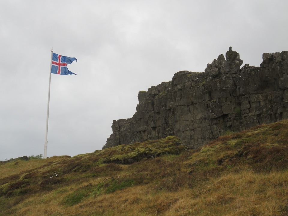 Icelandic flag on a pole near a rocky cliff.