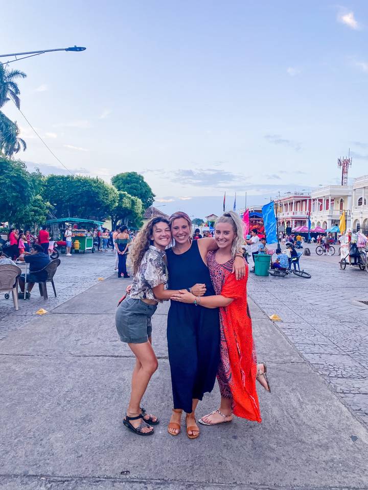 Three women posing together in a busy street market.