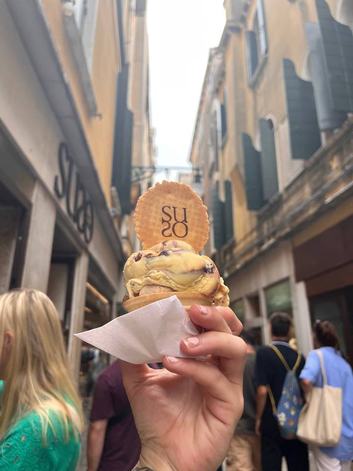 Close-up of a hand holding an ice cream cone with a street view.