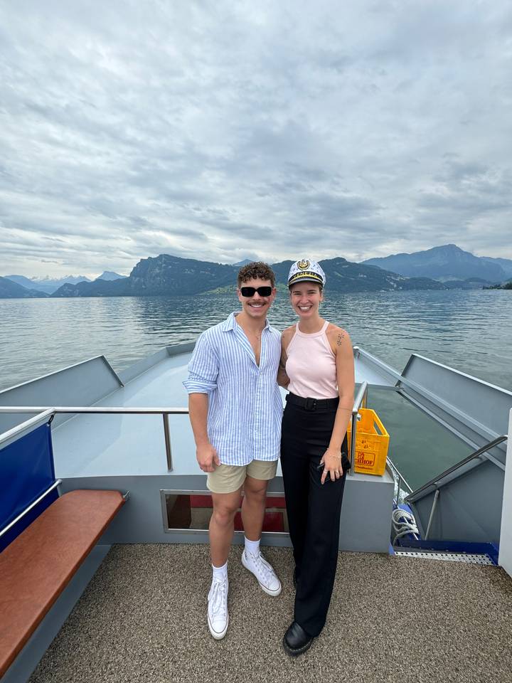 Two people smiling on a ship deck with water in the background.