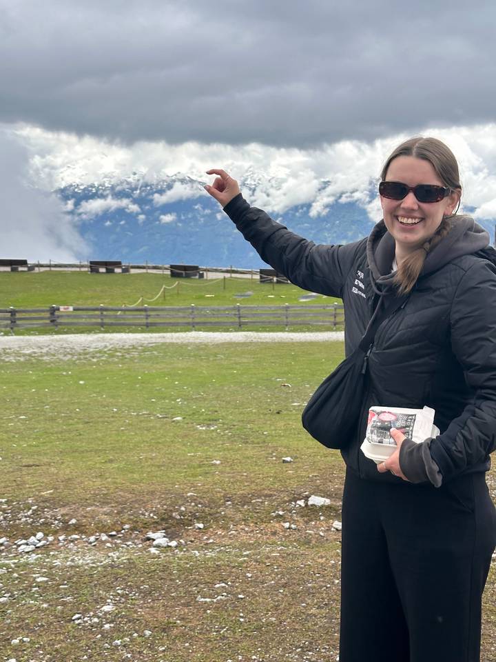 Smiling woman standing with mountains in the background, holding brochure.