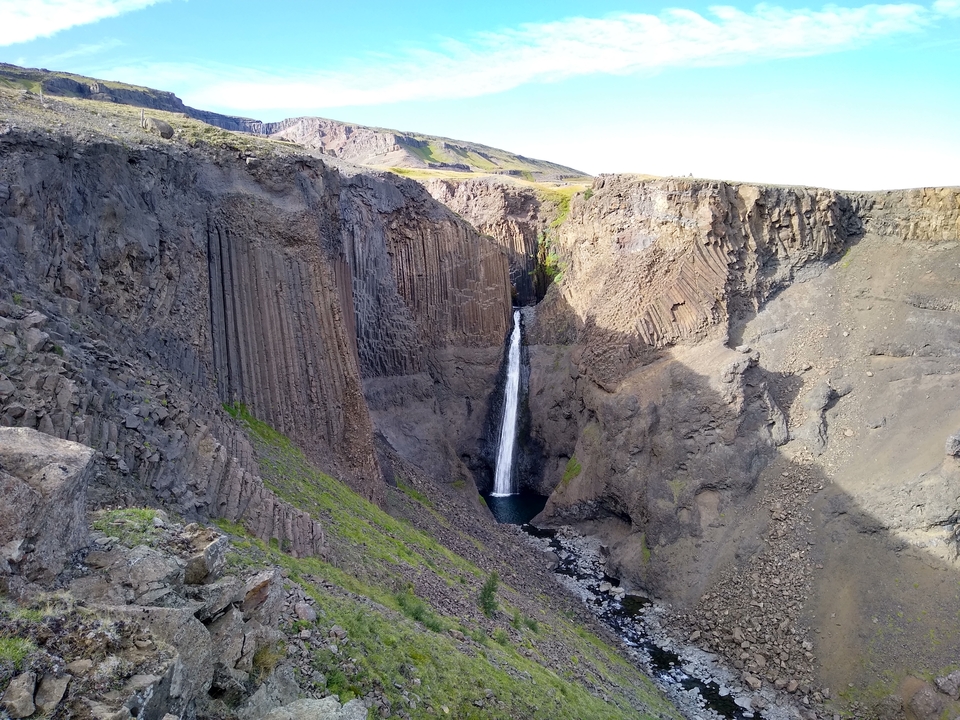 A tall waterfall in a narrow canyon with sheer rock walls.