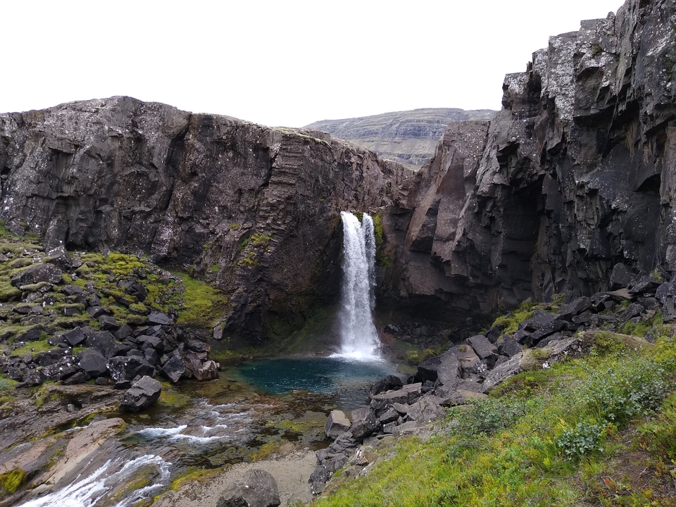 A waterfall cascading into a clear pool in a rocky enclosure.