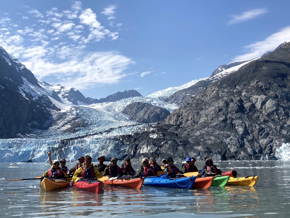 Group of people kayaking near a glacier with mountains in the background.