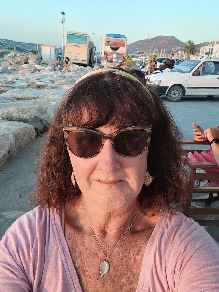 Woman wearing sunglasses posing with rocks in the background.