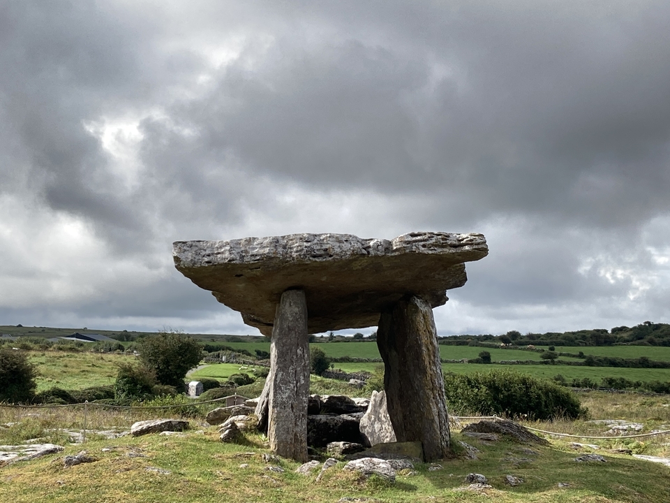 Ancient stone dolmen set in a green landscape with cloudy sky.