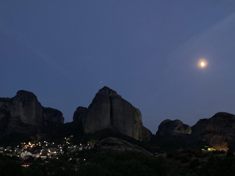 Vue nocturne de montagnes avec une pleine lune et une ville illuminée en contrebas.