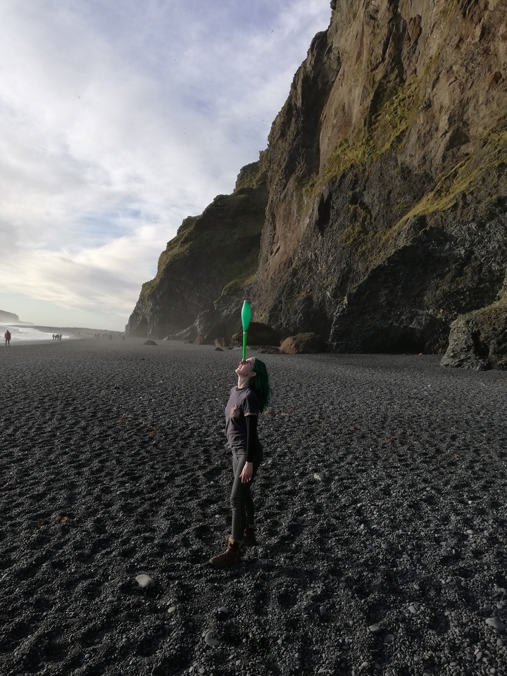 Person balancing a green bottle on forehead by the cliffs.