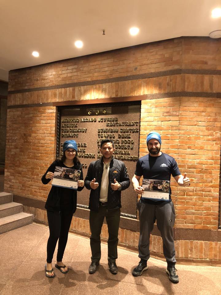 Trois personnes posant à l'intérieur avec un mur de briques en arrière-plan.