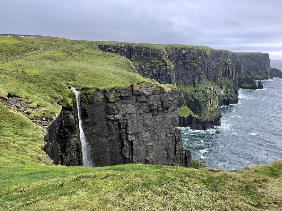 Falaises au bord de l'océan avec une cascade, sous un ciel couvert.