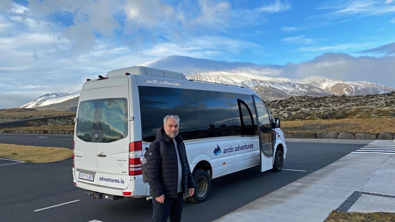 A man standing next to a tour van in a scenic area.