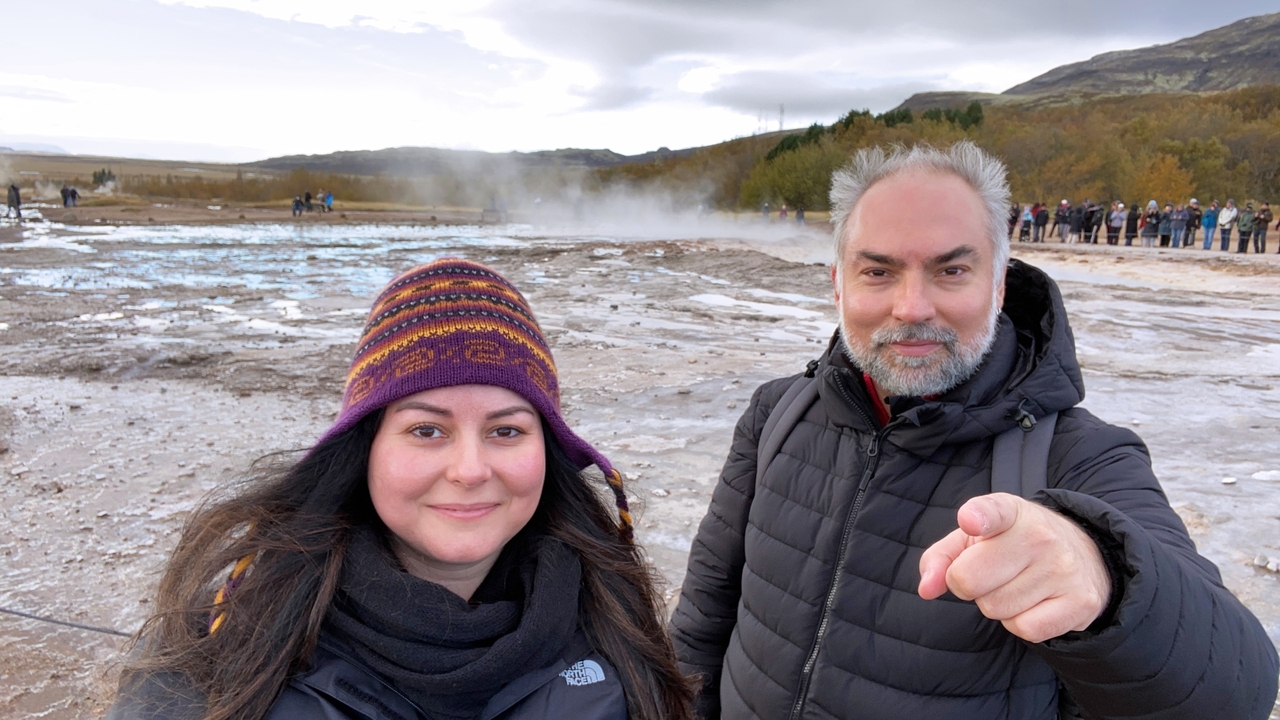 Two people in front of a geothermal area with steam.