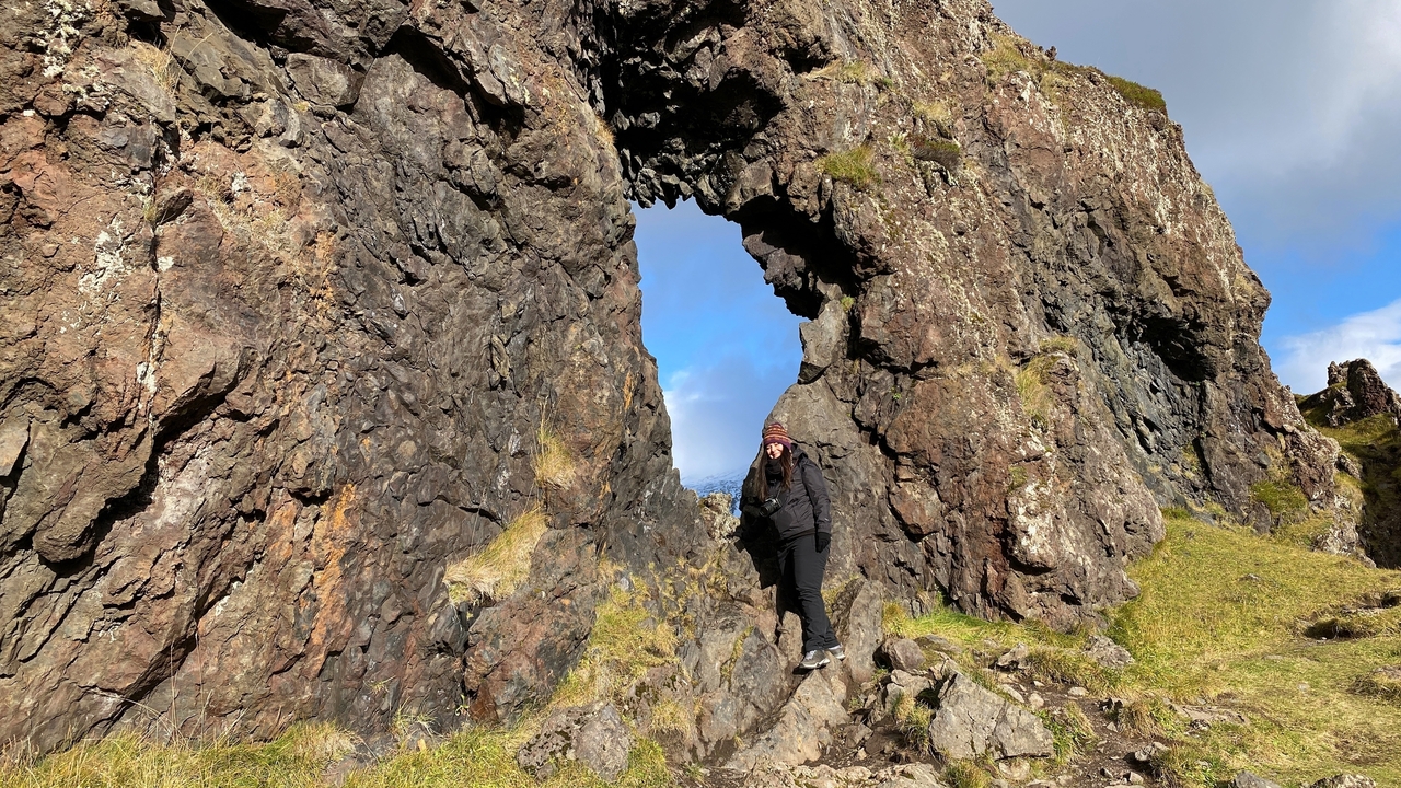 A person standing next to a rock with a natural hole.