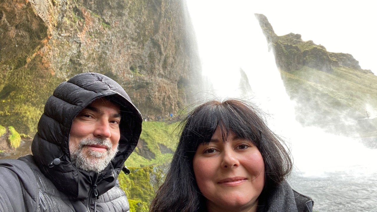 Two people in front of a large waterfall with mist.