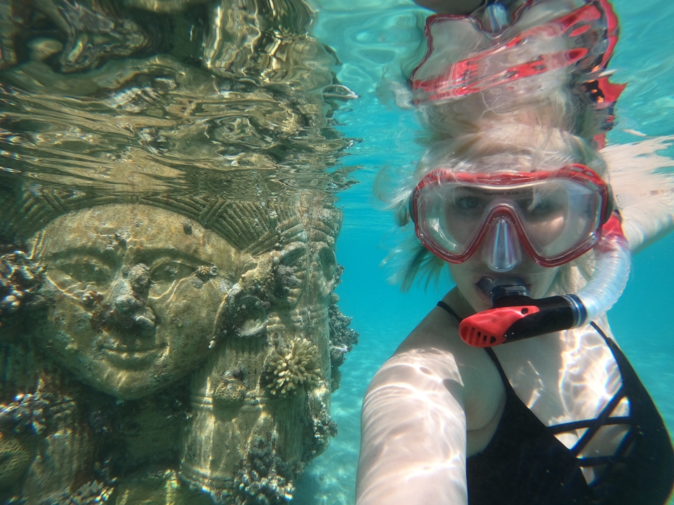 Person snorkeling near an underwater statue.