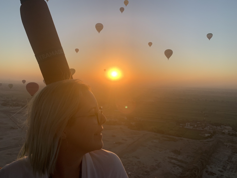 Person in hot air balloon during sunrise with other balloons in the background.