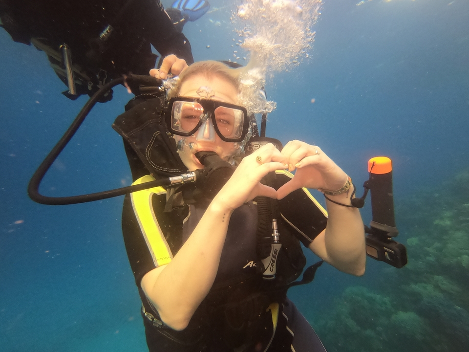 Person underwater scuba diving, making a heart with hands.