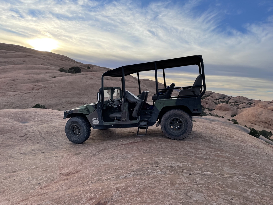 A large off-road vehicle parked on a rocky desert landscape during sunset.