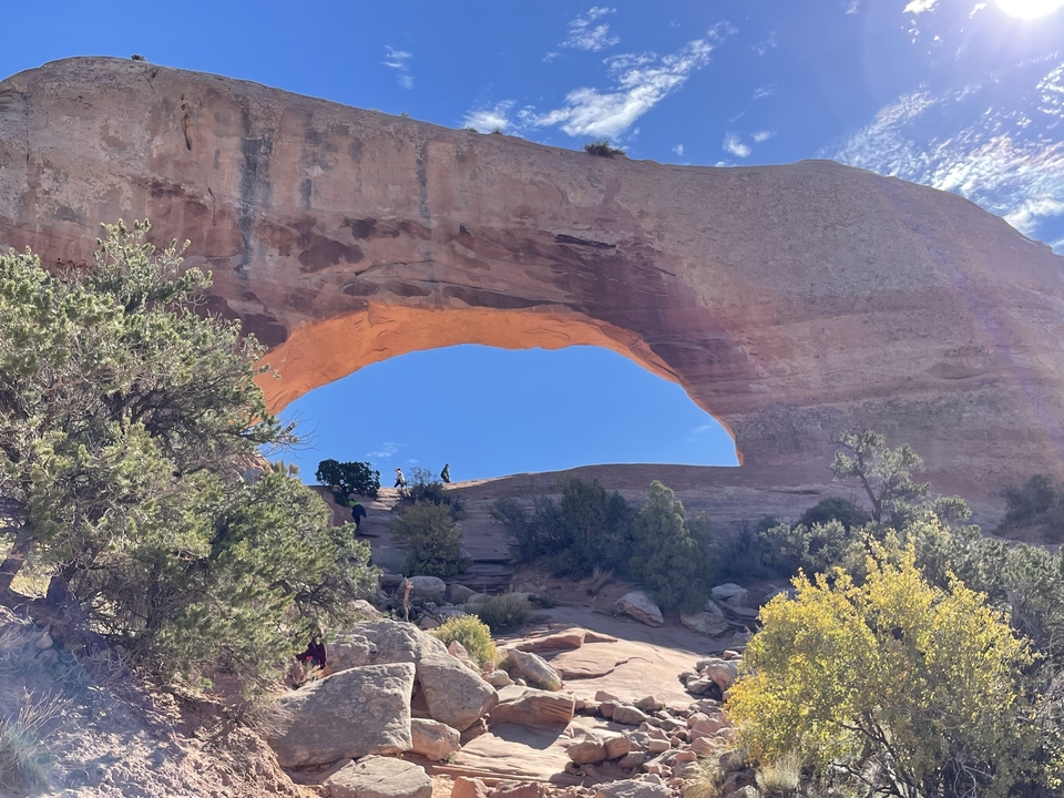 A natural arch formation with a clear blue sky and desert landscape.
