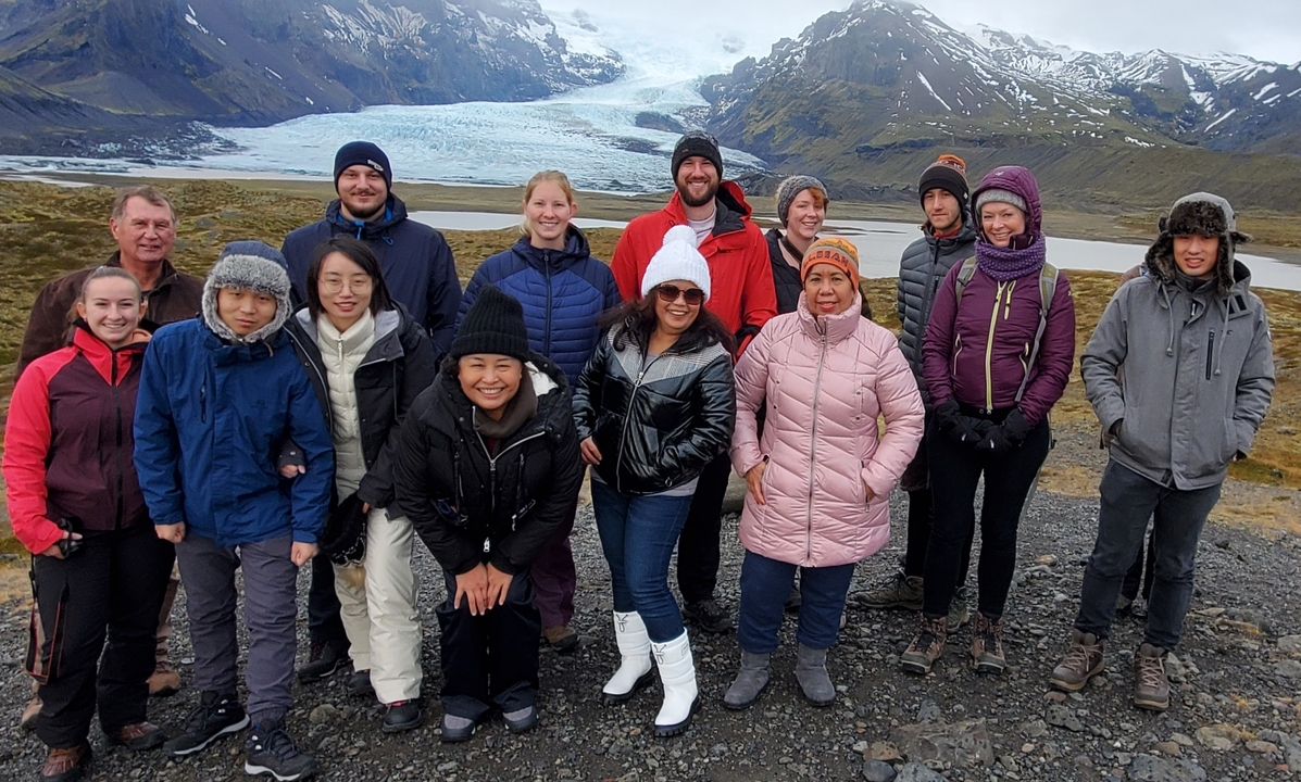 Group of 14 people posing in front of a distant glacier.