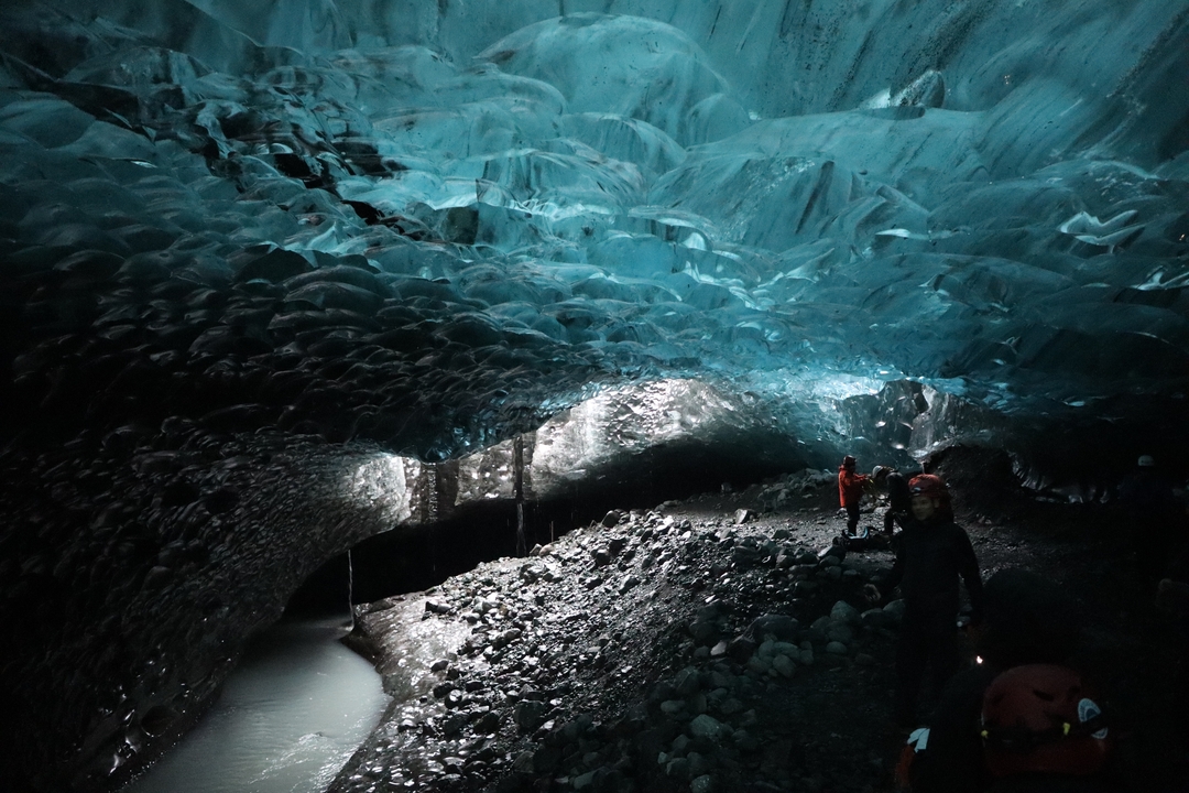 Des personnes explorant une grotte de glace avec un éclairage dramatique.