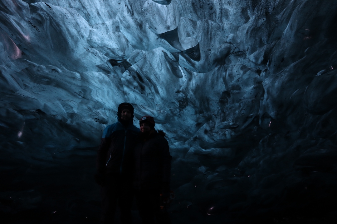 Des personnes en silhouette sous une grotte de glace avec une teinte bleuâtre.