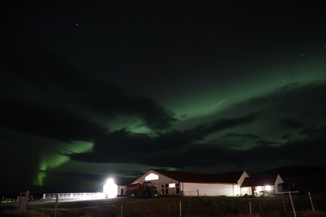 Aurores boréales au-dessus d'une maison dans la campagne la nuit.