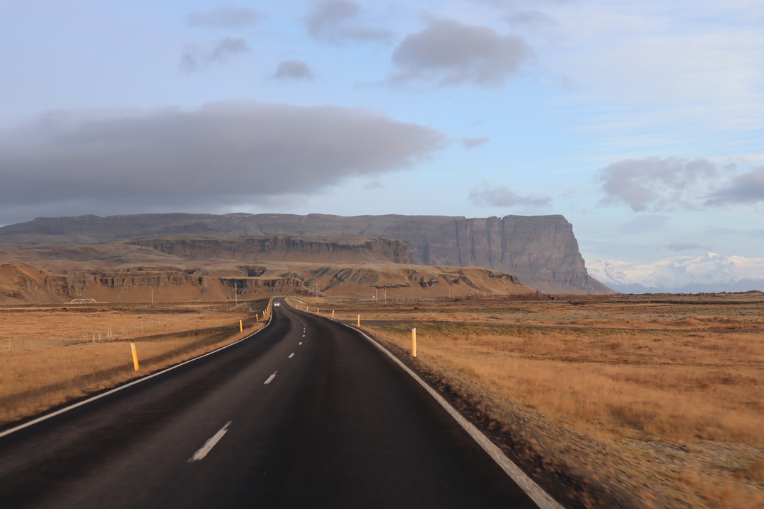 Route ouverte menant aux montagnes sous un ciel partiellement nuageux.