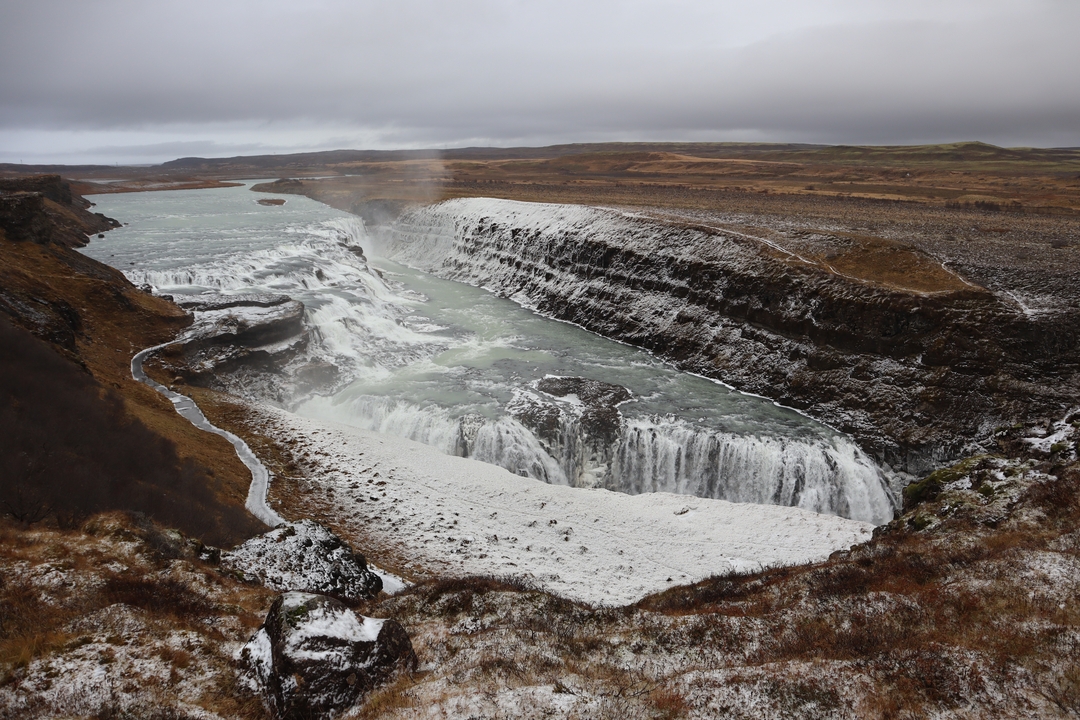 Waterfall in a rugged landscape, partly covered in snow.