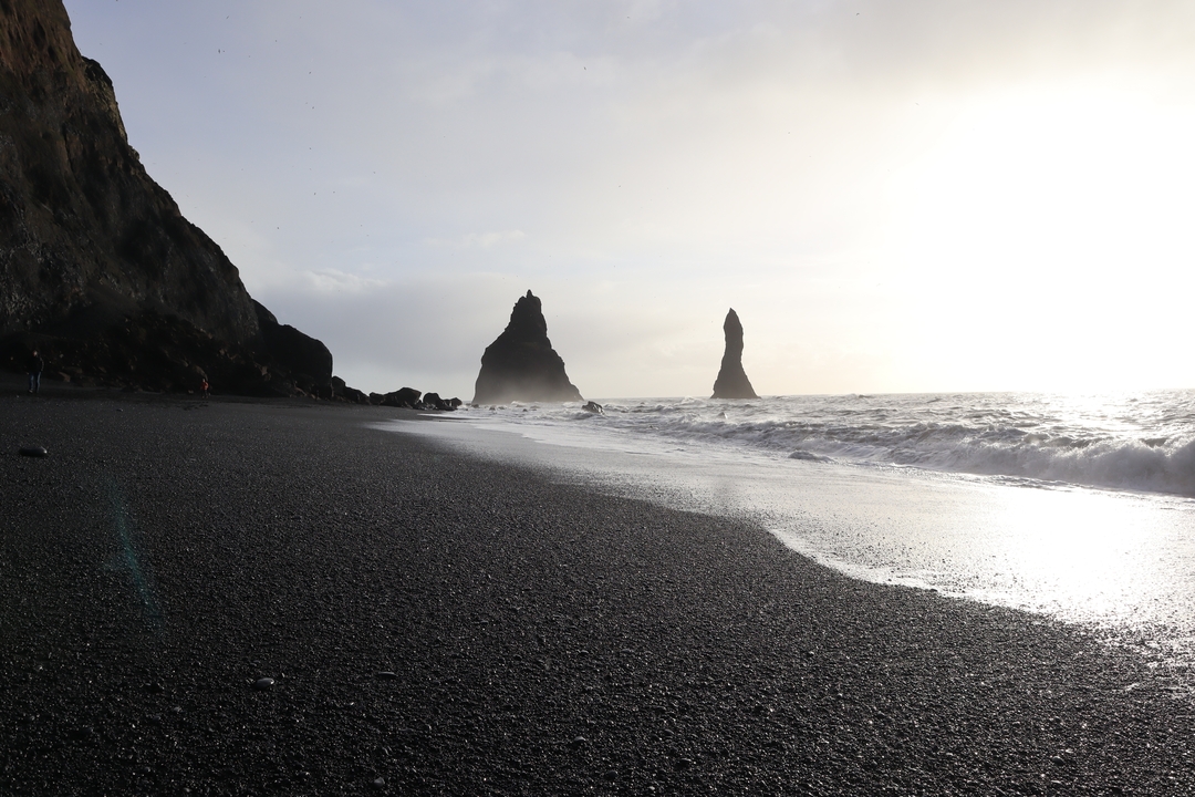 Plage de sable noir avec des formations rocheuses saisissantes et des vagues qui se brisent.