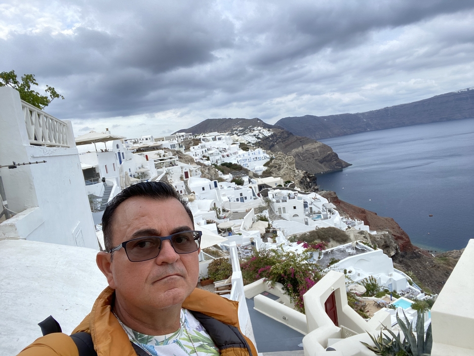 Un homme prenant un selfie avec une vue panoramique des falaises et des bâtiments blancs de Santorin.