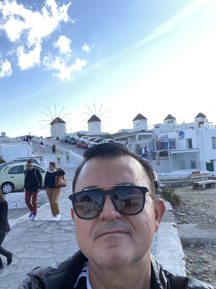 Un homme prend un selfie avec les célèbres moulins à vent de Mykonos en arrière-plan.
