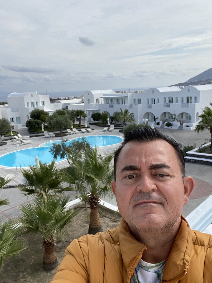 Un homme prenant un selfie devant des bâtiments blancs et une piscine, typique de Santorin.