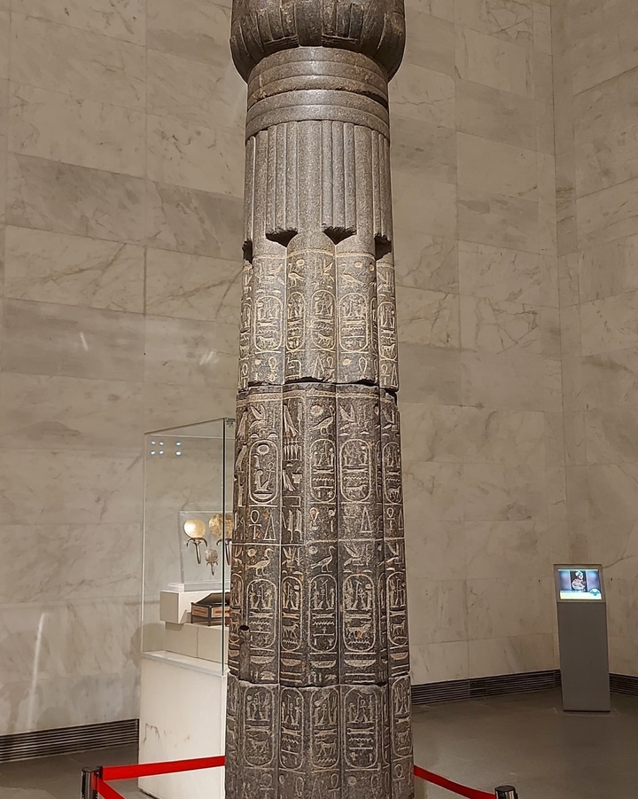 Ancient Egyptian stone pillar with hieroglyphs in a museum setting.