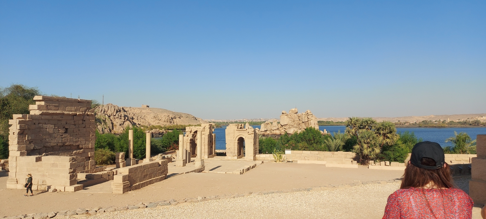 Ruined stone structures near a river with a person observing.