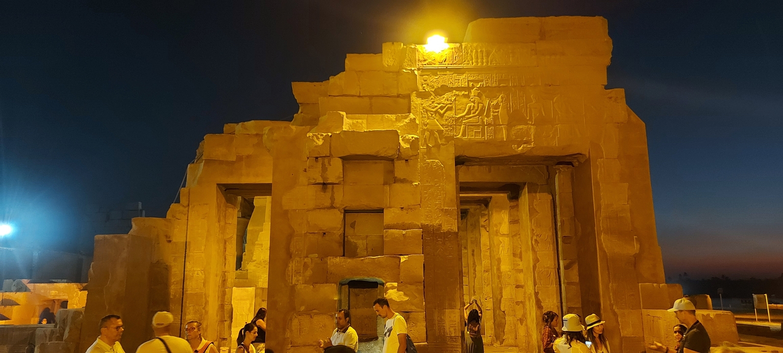 Night view of an illuminated ancient temple with visitors.