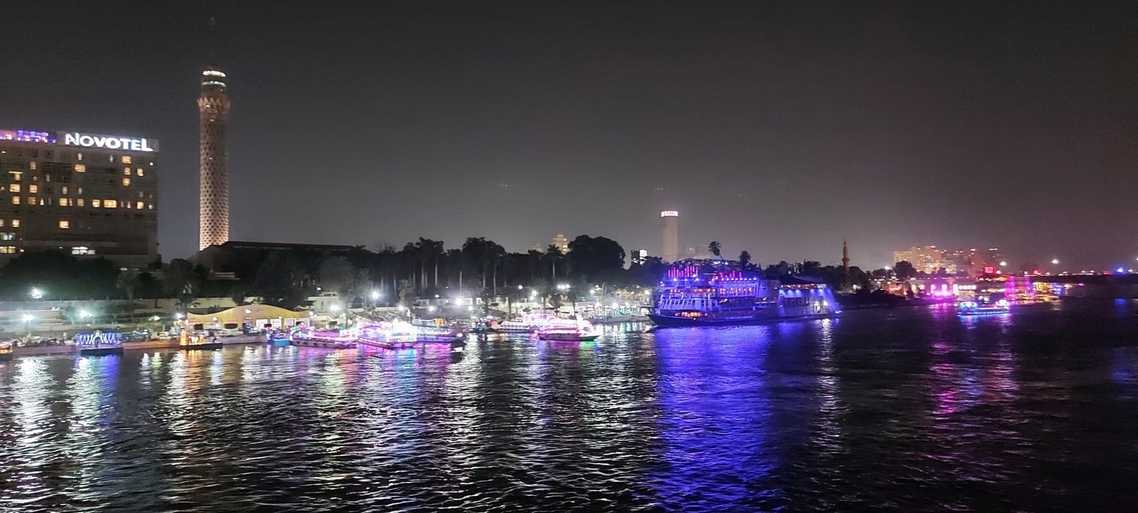 Illuminated riverside with colorful lights and tall buildings.