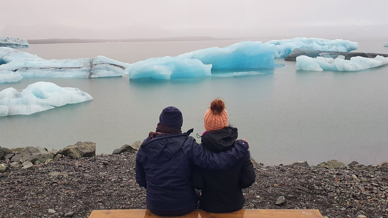 Deux personnes assises sur un banc regardant des icebergs flottants.