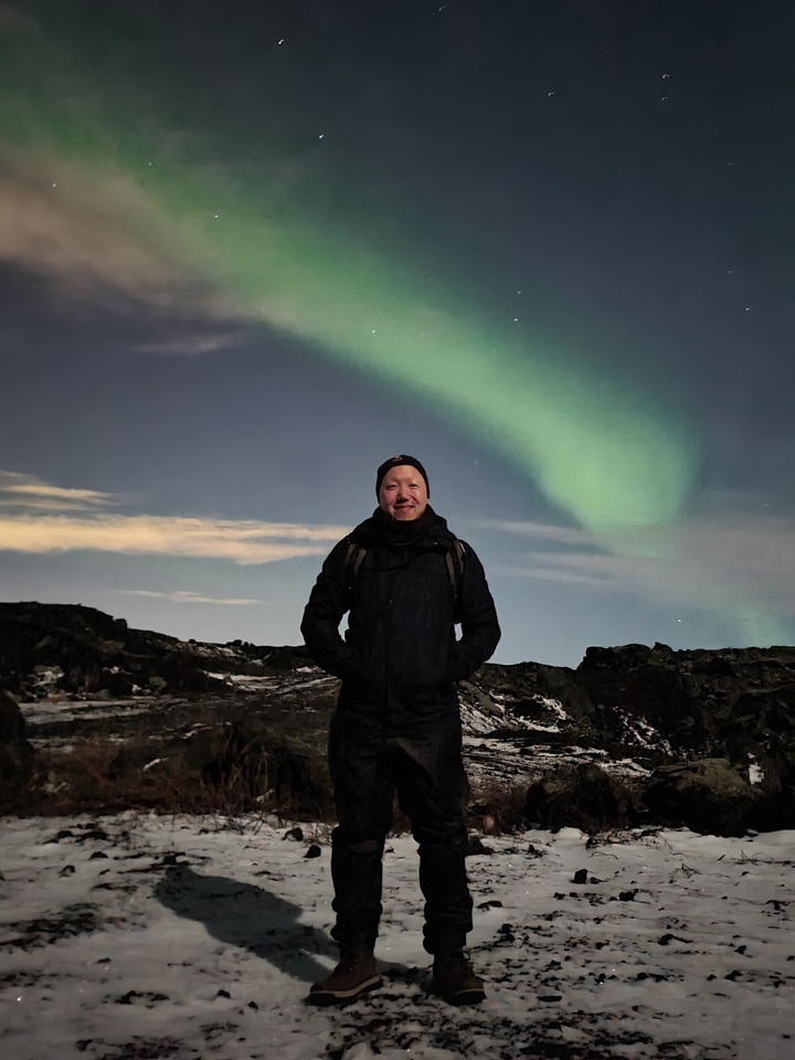 Homme debout sous les aurores boréales dans une zone rocheuse.