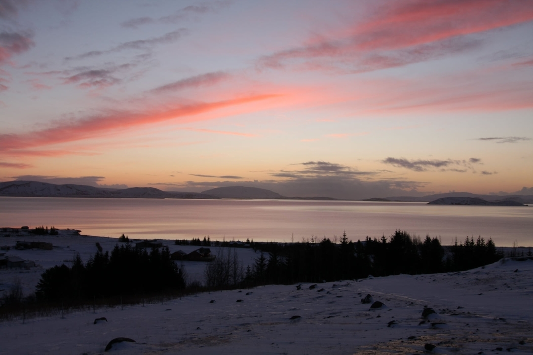 Vue sereine sur le lac avec des montagnes enneigées au coucher du soleil.