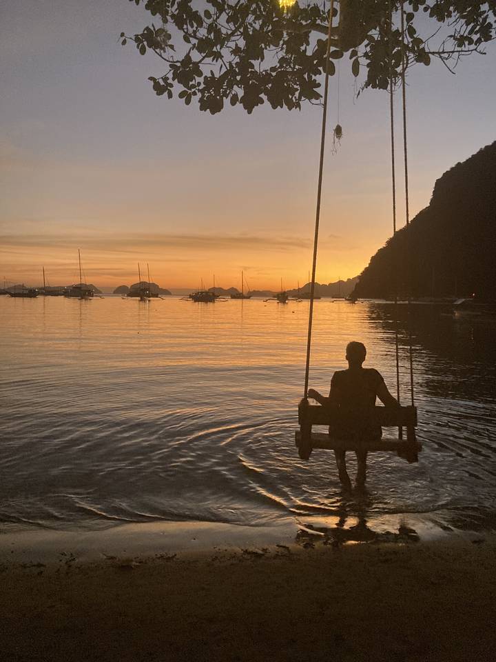 Person on a swing over the water, with a sunset view.