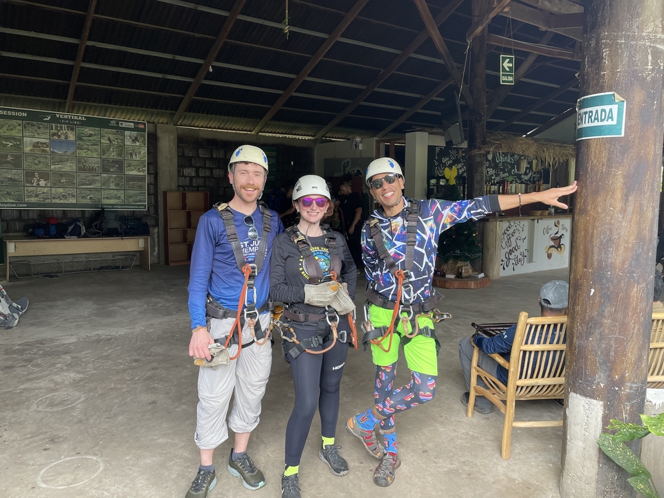 Three people wearing climbing gear posing indoors under a roof structure.