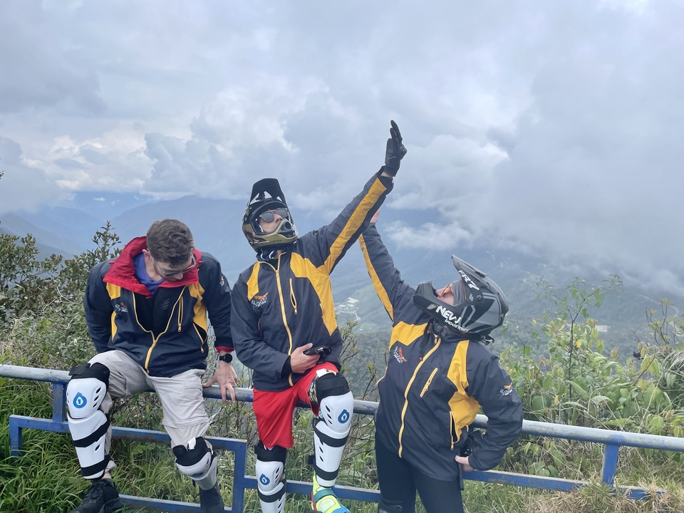Three people in colorful jackets and helmets posing playfully with a mountainous background.