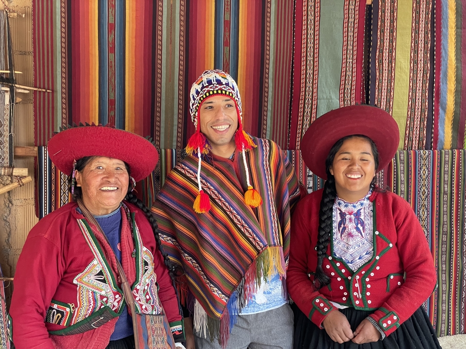 Three people dressed in traditional attire in front of colorful textiles.