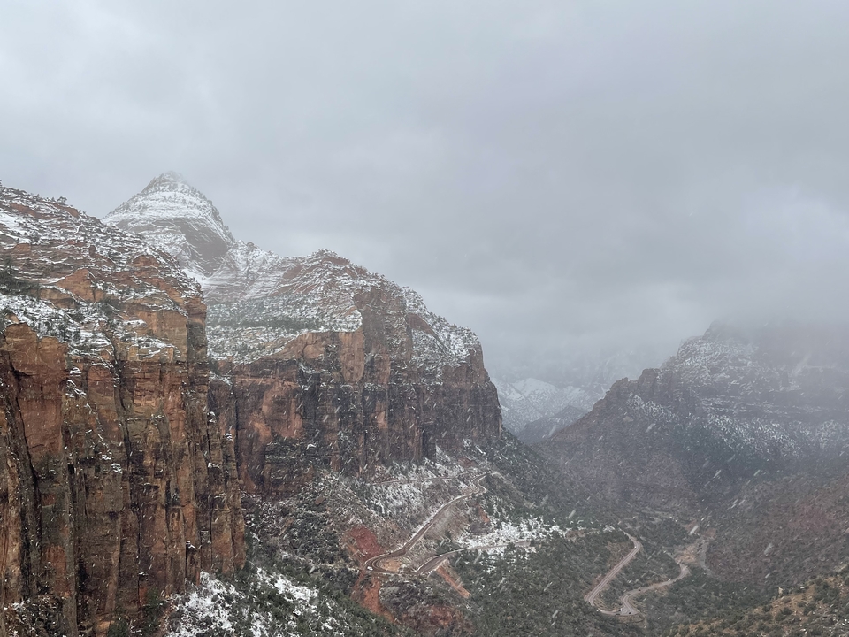 Snow-covered red rock cliffs under a cloudy sky.