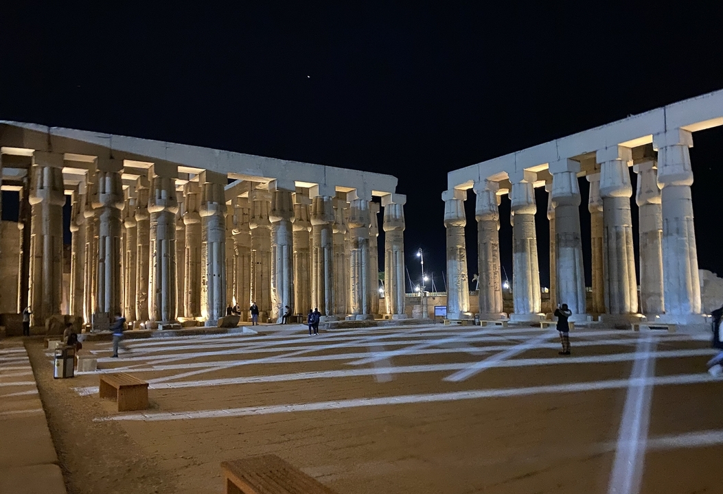 Lit ancient columns at night with people observing.
