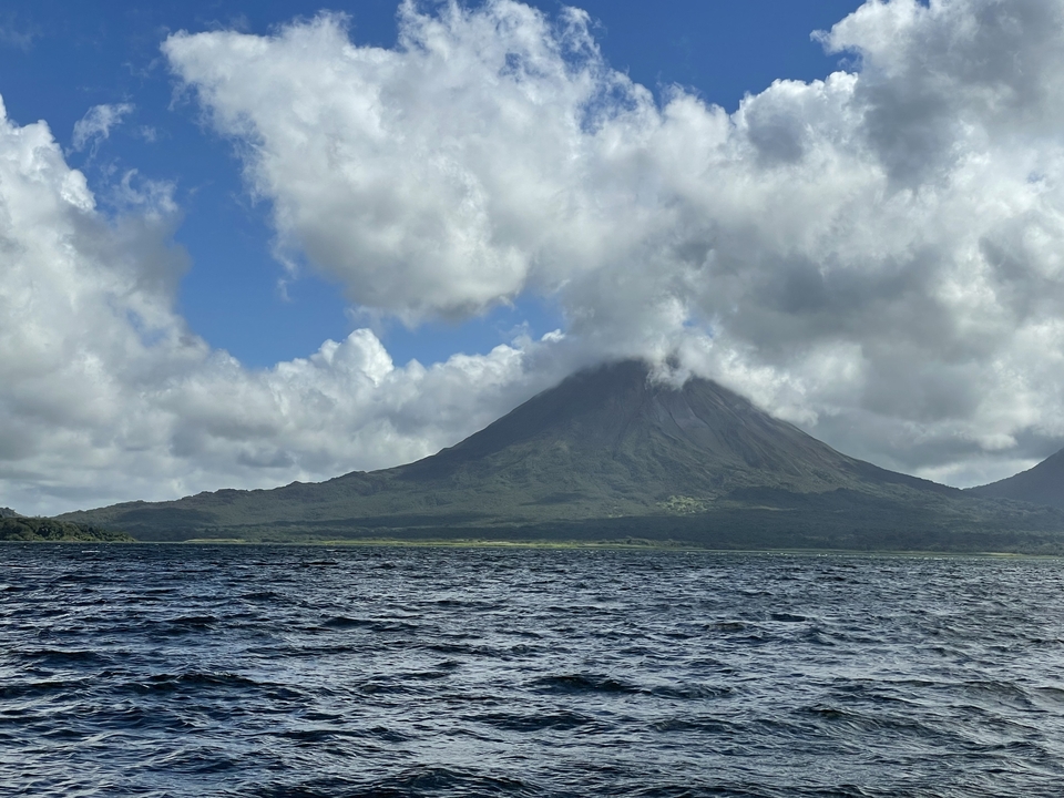 Arenal Volcano towering over a lake under a cloudy sky.