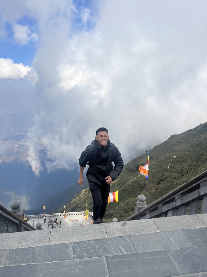 Person posing on a mountain with colorful flags and sky in the background.