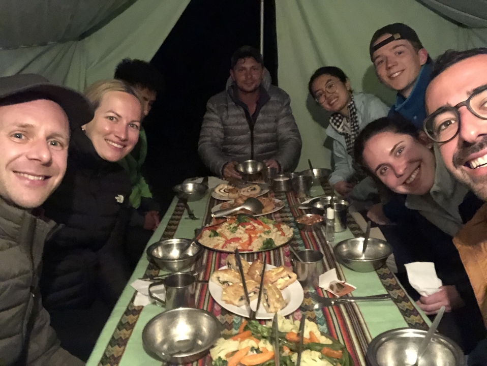 Group of people dining outdoors with food on the table.