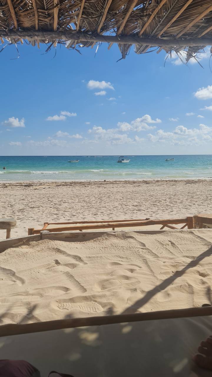 Sandy beach with turquoise water and clouds above.